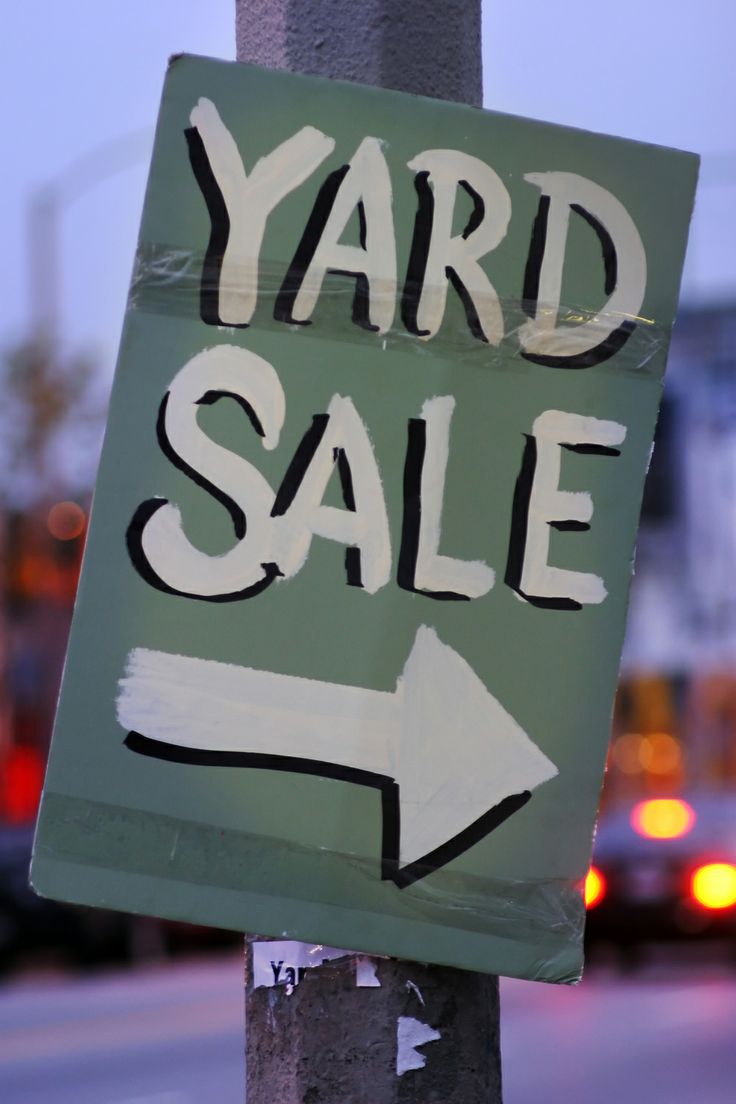 a yard sale sign with an arrow pointing to the right on a pole in front of a city street