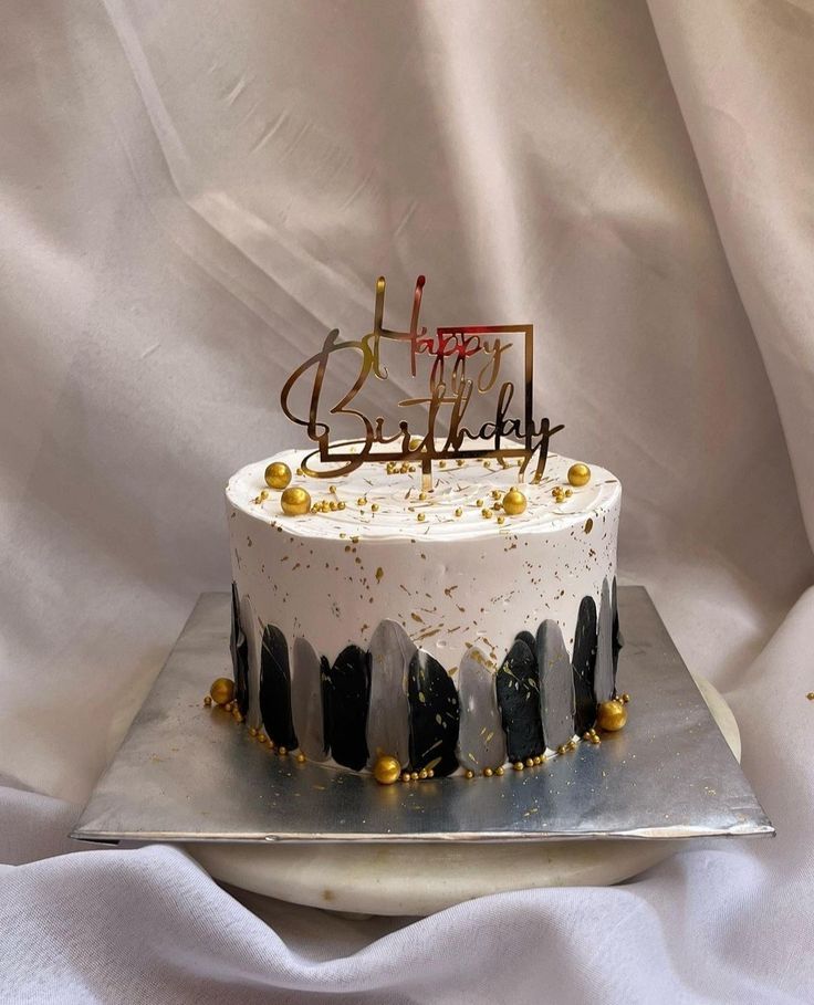 a white and black birthday cake with gold sprinkles is on a silver platter