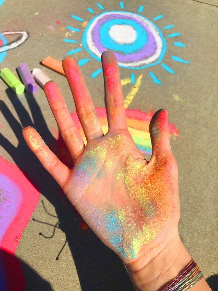 a person's hand covered in colored powder next to crayons and chalk