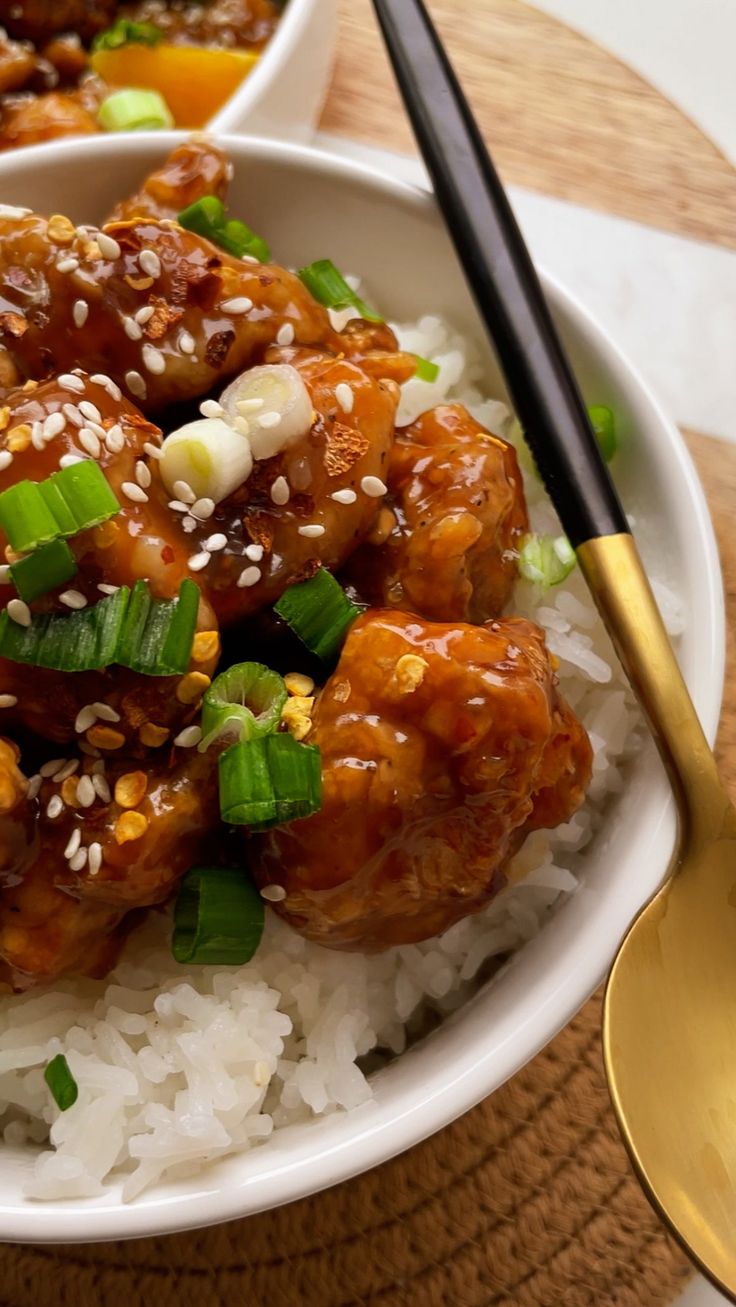 two white bowls filled with rice and meat on top of a wooden table next to chopsticks