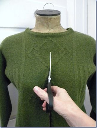 a person is holding scissors in front of a green sweater on a mannequin