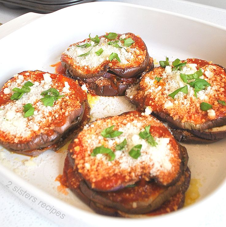 four stuffed mushrooms in a white dish with parmesan cheese and green garnish