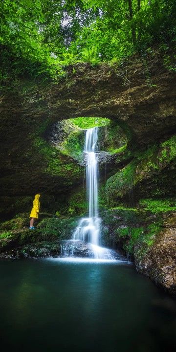 a person standing in front of a waterfall with a yellow raincoat over their head