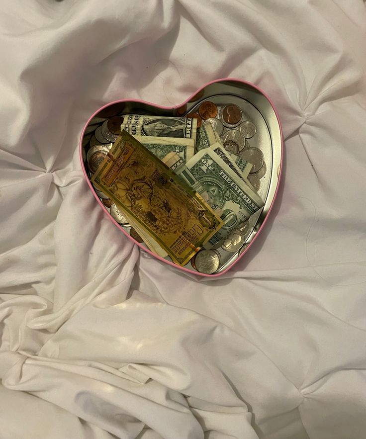 a heart shaped box filled with money on top of a white sheet