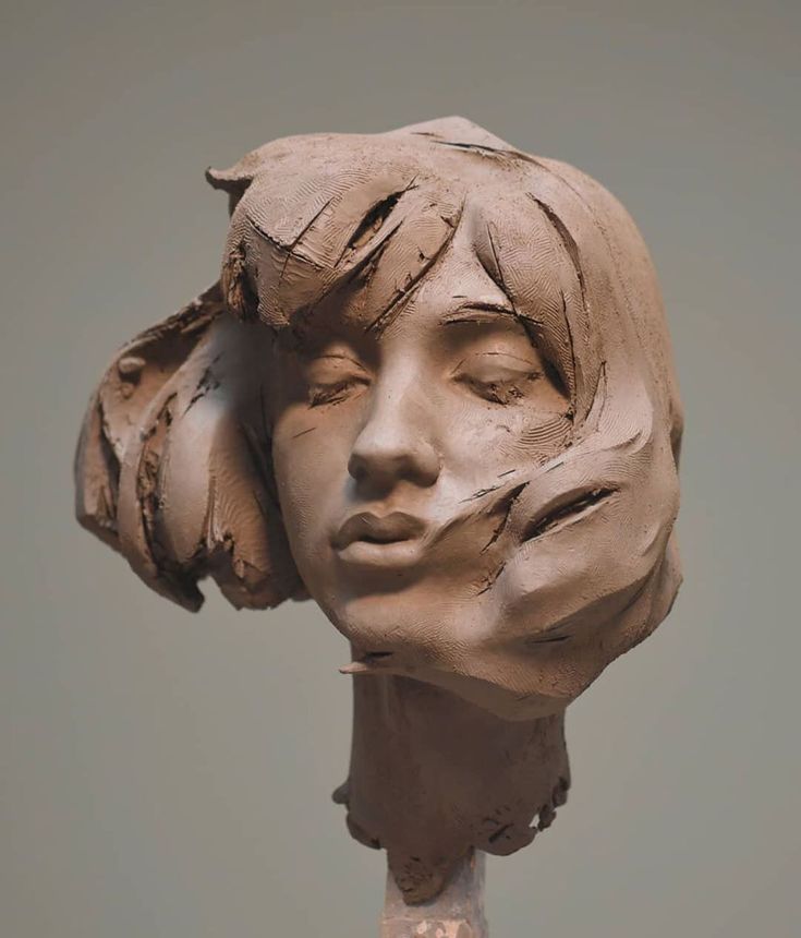 a clay sculpture of a woman's head with her hair pulled back and eyes closed