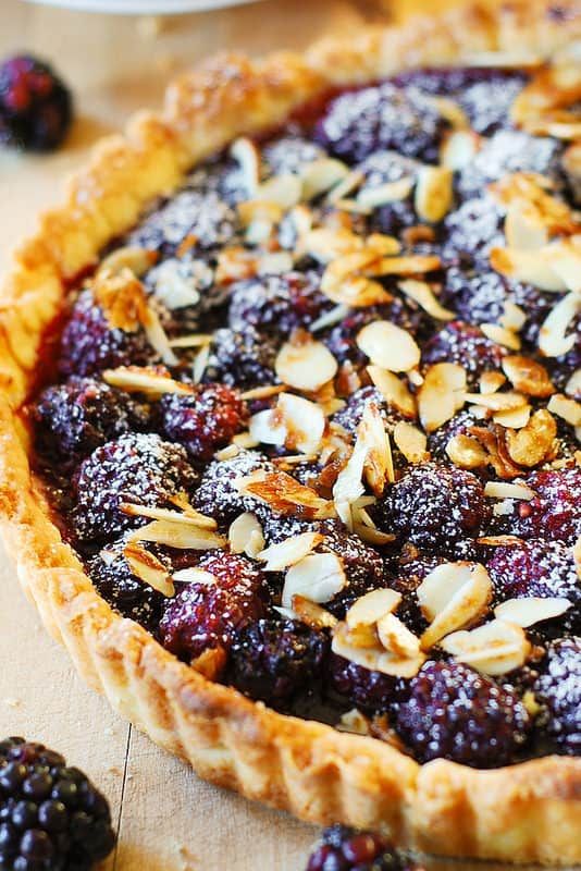 a pie with berries and almonds on it sitting on top of a wooden table