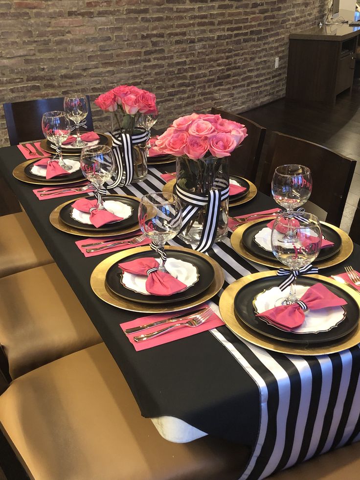 the table is set with black and gold plates, pink flowers, and napkins