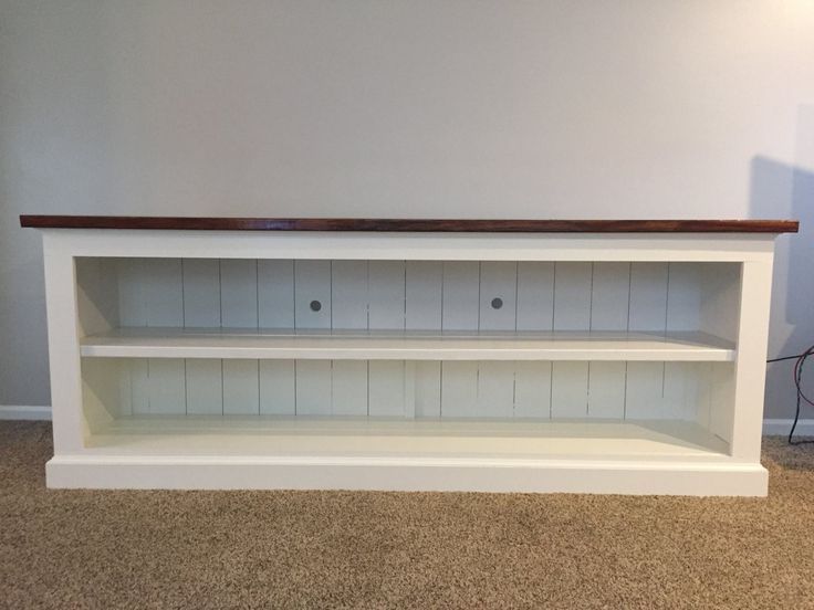 a white entertainment center with wooden shelves in an empty room