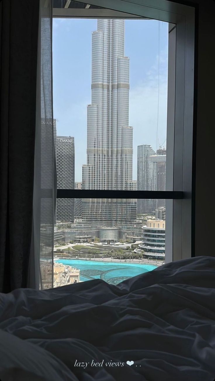 a bed sitting in front of a window next to a tall building near the ocean