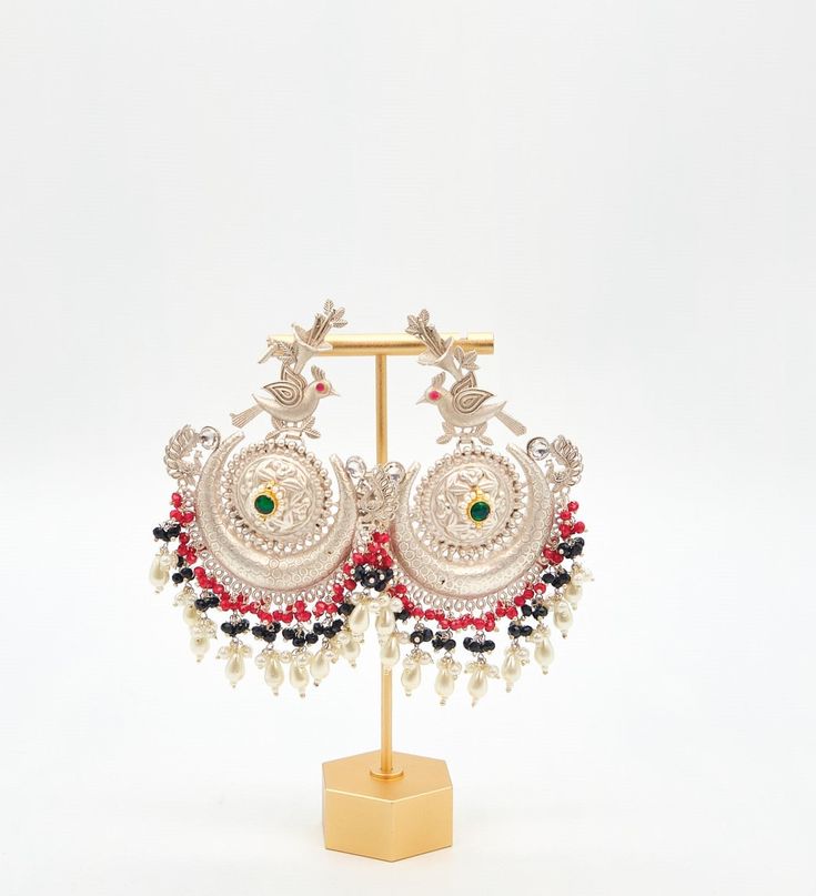 Upgrade your festive look with silver-coated pachi kundan peacock earrings featuring tribal designs and pearl tassels. Earrings Length: Approx. 4" Weight of each earring: 25 gms Brass as the base metal Availability: In-Stock *Color may vary slightly due to light condition & photography. Jewelry Care: Keep away from moisture. Allow perfumes and lotion to dry before wearing. Store in jewelry pouch. Clean only with soft lint free cloth. Silver Chandbali Earrings For Puja, Silver Latkans Earrings For Puja, Silver Earrings For Puja And Diwali, Silver Earrings For Diwali Puja, Traditional Pearl Earrings For Festive Celebrations, Traditional Red Chandbali Pearl Earrings, Traditional Festive Drop Pearl Earrings, Traditional Peacock Design Danglers For Party, Festive Red Temple Jewelry Pearl Earrings