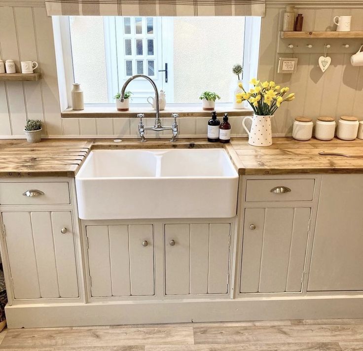 a white kitchen sink sitting under a window next to a counter top with yellow flowers