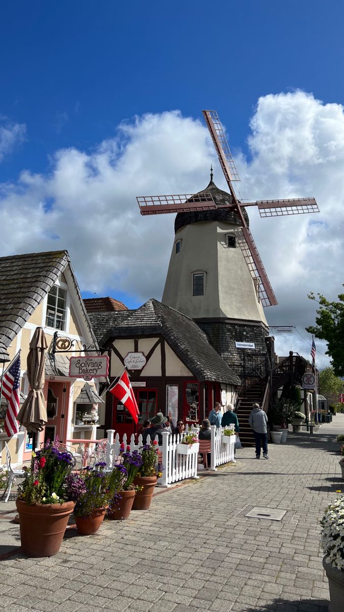 a windmill sits in the middle of a town with many flowers and potted plants