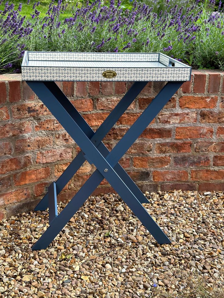 a table with a tray on it sitting in front of a brick wall and purple flowers