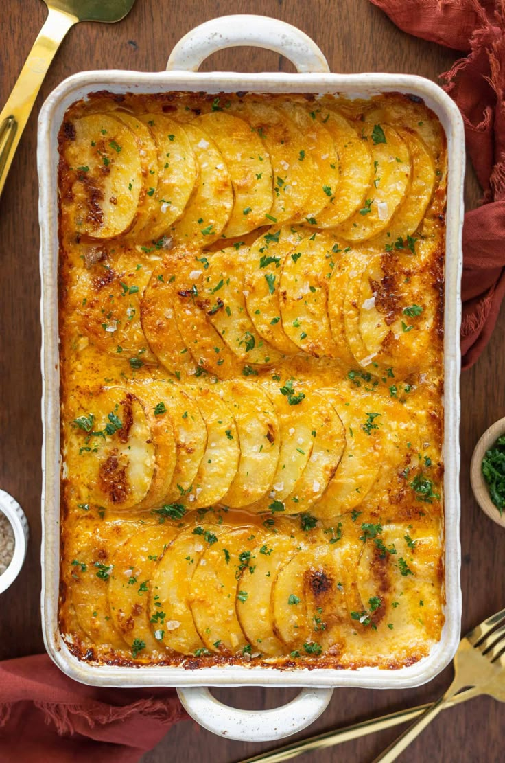 a casserole dish filled with potatoes and topped with parsley on a wooden table