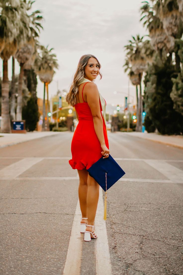 a woman in a red dress is holding a blue purse and standing on the street