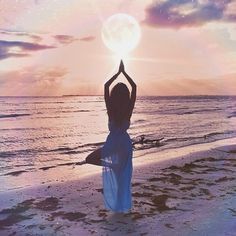 a woman is standing on the beach with her arms in the air and looking at the sky