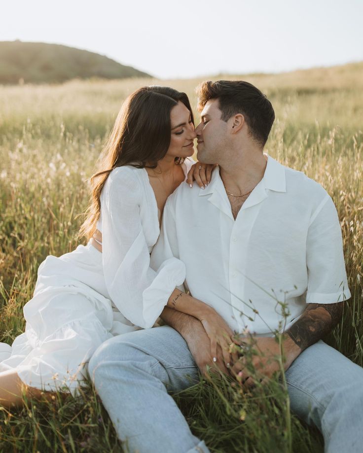 a man and woman are sitting in the grass, one is holding his face to the other's chest