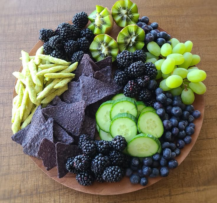 a wooden plate topped with fruit and veggies on top of a brown table