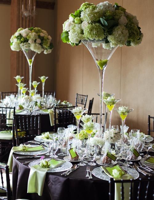 the tables are set up with green and white flowers in tall vases on them