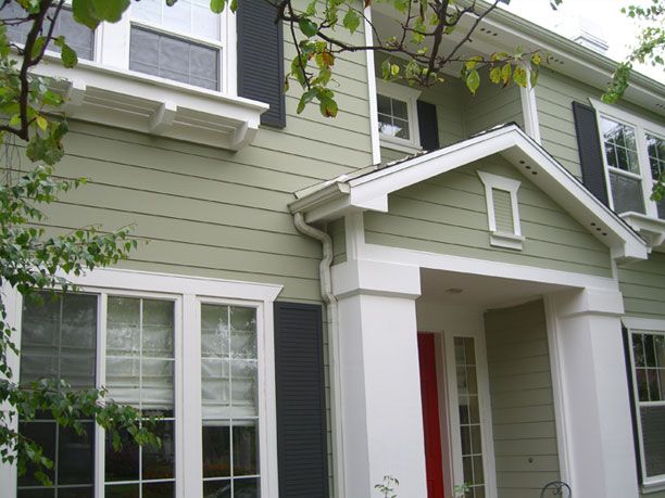 a green house with white trim and black shutters on the front door is shown