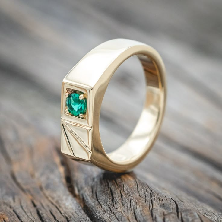 a gold ring with a green stone in the center sitting on a wooden surface next to a piece of wood