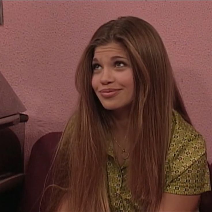 a woman with long brown hair sitting on a purple couch next to a pink wall