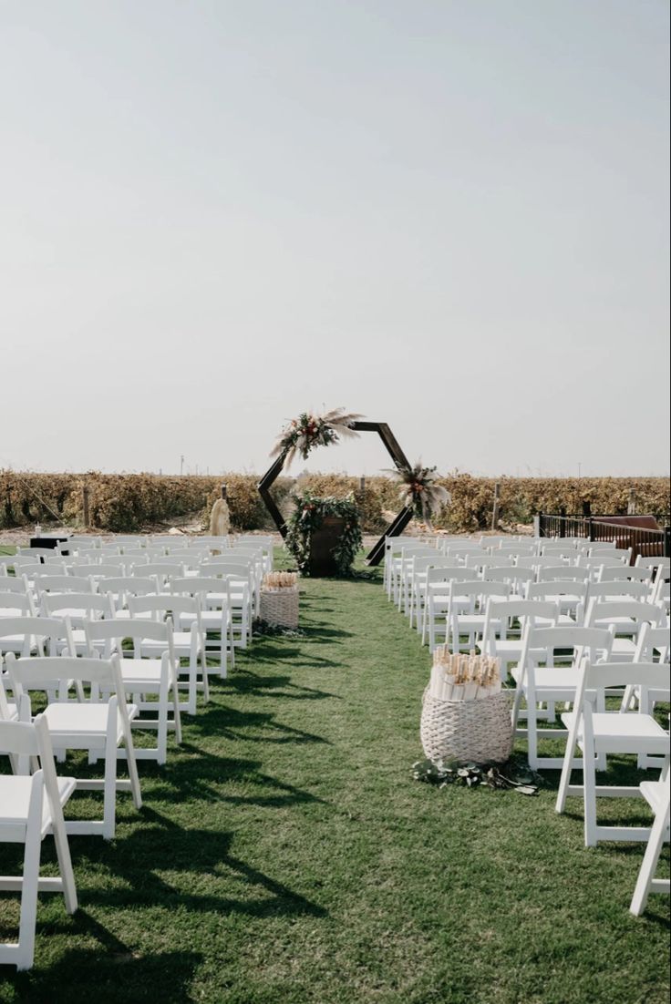 an outdoor ceremony setup with white chairs and wicker baskets on the grass in front of it