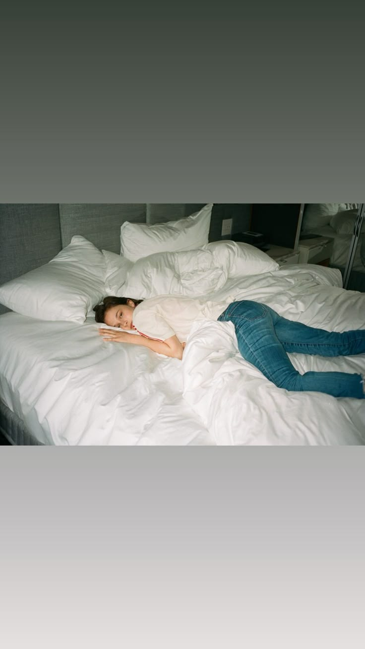 a woman laying on top of a bed covered in white sheets