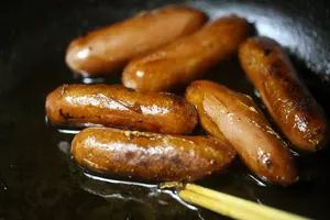 several sausages are cooking in a pan with a yellow stick next to them on the stove