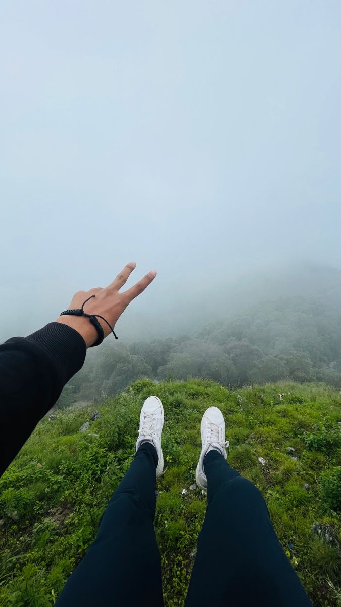 two people standing on top of a grass covered hill with their hands in the air