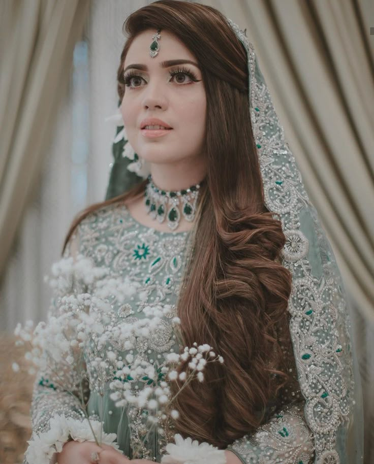 a woman with long brown hair wearing a green and white wedding dress, holding flowers in her hand