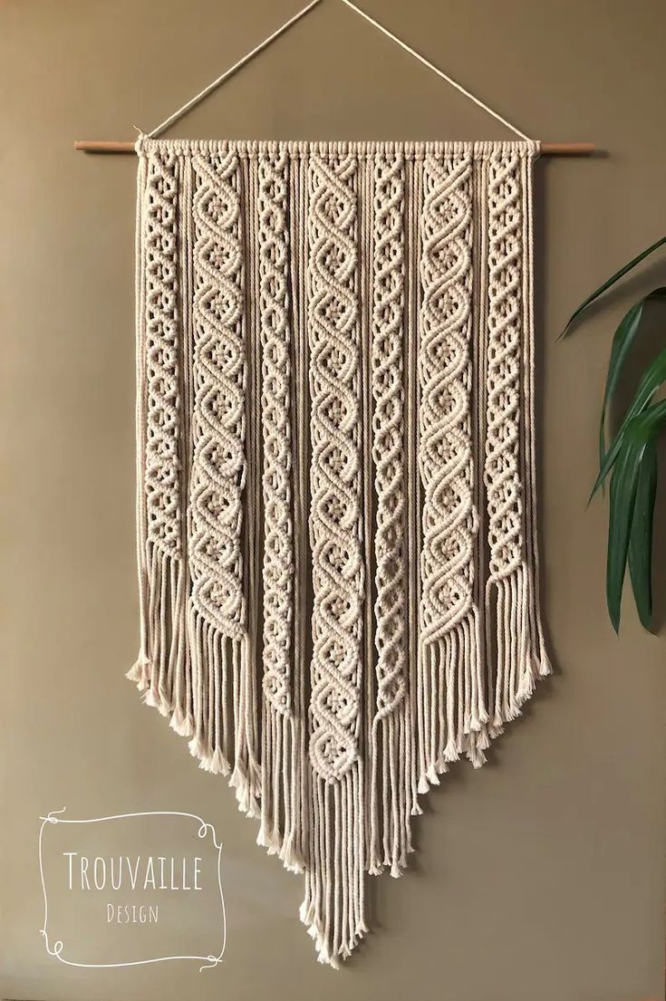 a macrame wall hanging on the wall next to a potted plant