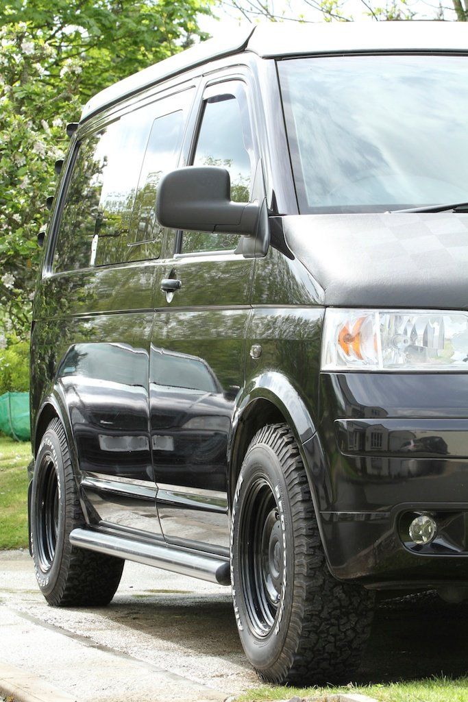 the black van is parked on the side of the road in front of some trees