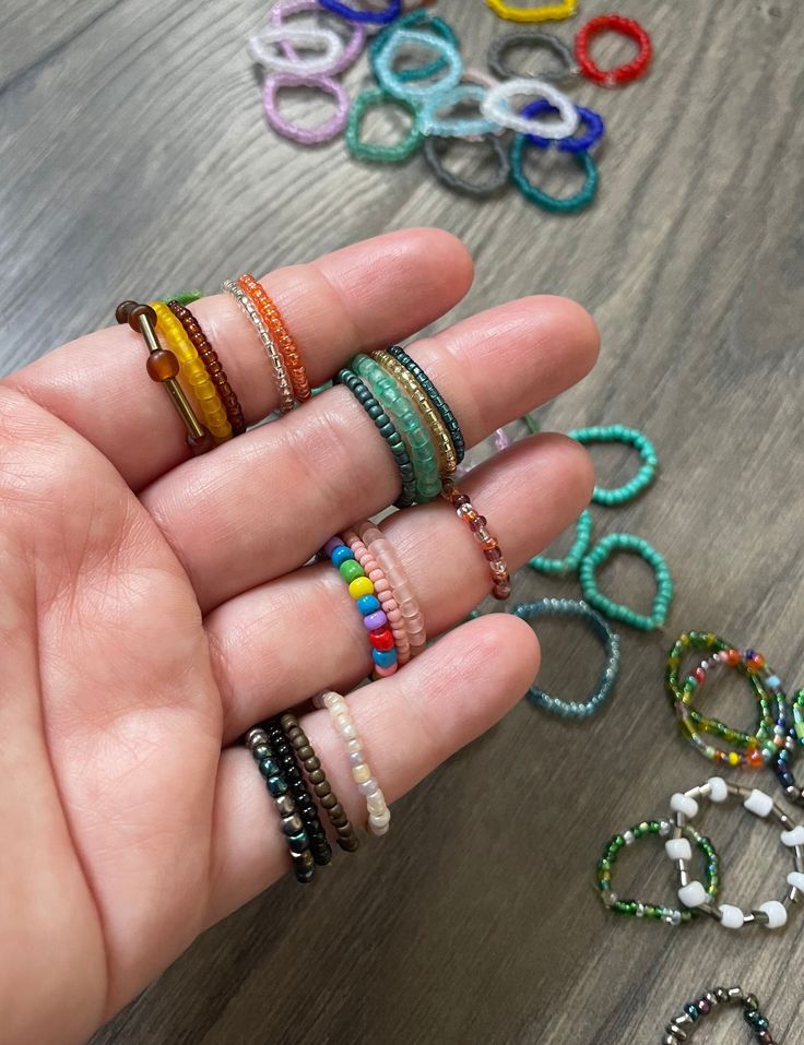 a person's hand holding several different colored bracelets on top of a wooden table