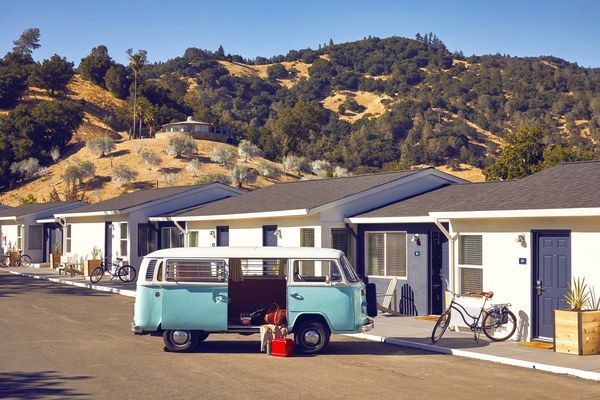 an old vw bus parked in front of some houses with mountains in the background