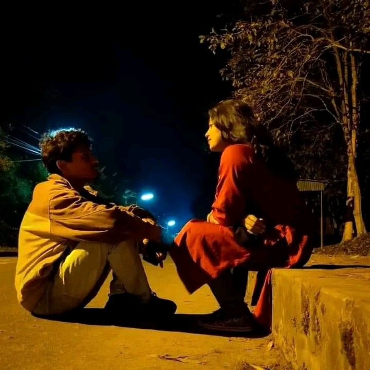 a man and woman sitting on the side of a road at night talking to each other