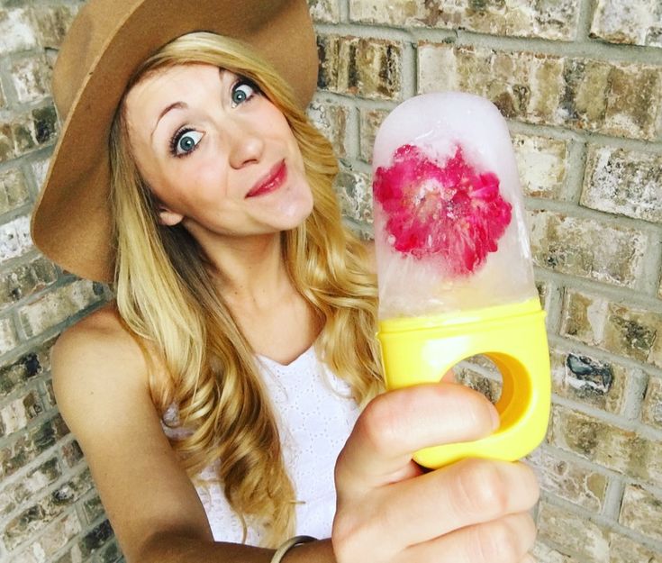 a woman is holding an ice cream cone with pink frosting on it and wearing a cowboy hat