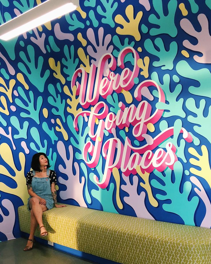 a woman sitting on top of a bed in front of a colorful wall with the words we are going places