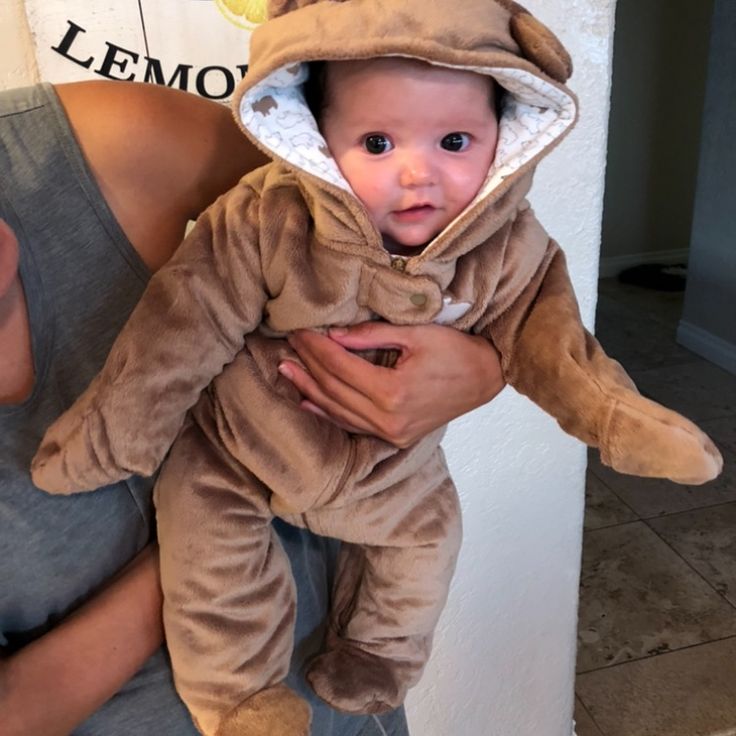 a man holding a baby dressed in a bear costume while wearing a hoodie on top of his head