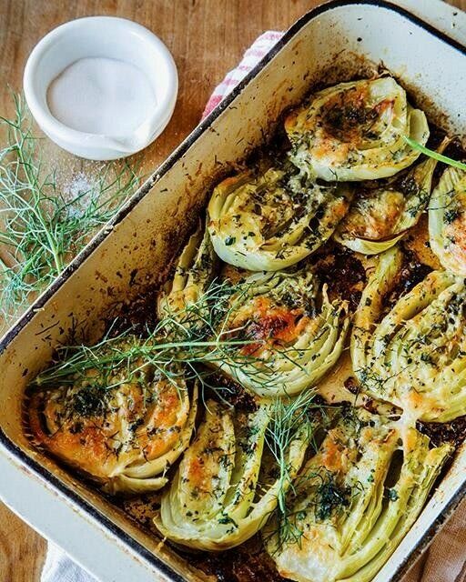 an oven filled with cooked artichokes on top of a wooden table next to utensils