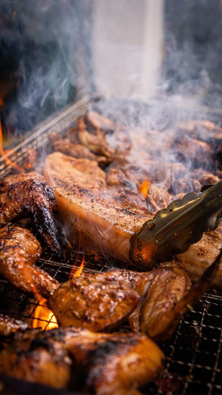 chicken and meat cooking on the grill with tongs sticking out of it's side