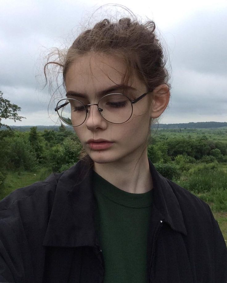 a woman wearing glasses looking down at her cell phone while standing in front of the camera