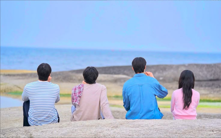 four people sitting on top of a rock looking out at the ocean