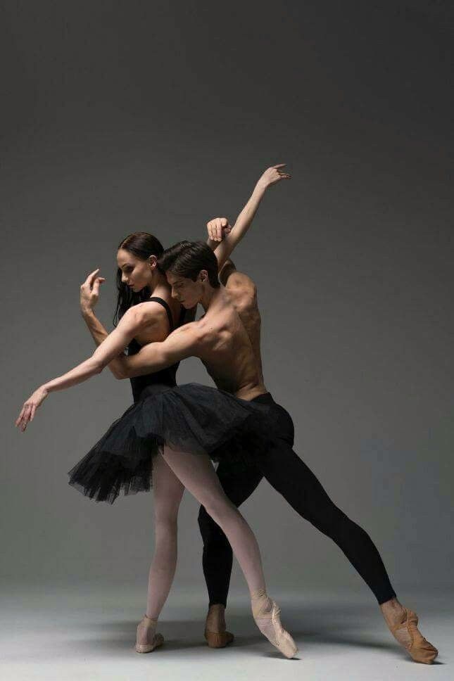 two ballerinas in black tutus and ballet shoes, one is holding the other's leg