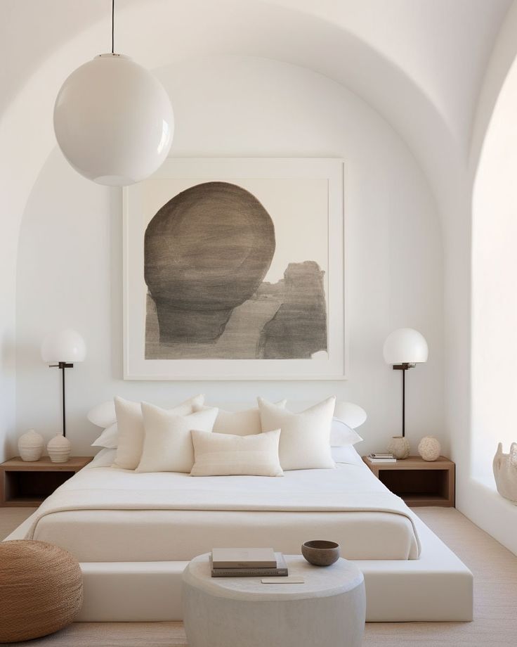 a white bed sitting under a painting in a bedroom next to two tables and lamps