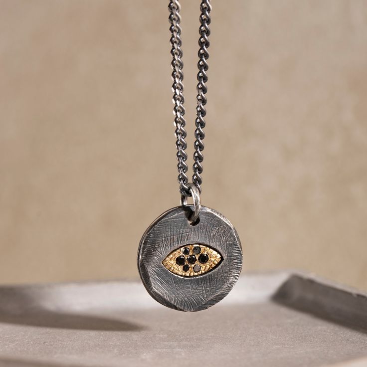 "A brutalist sterling silver disc necklace with an evil eye for men and women in black oxidized silver. This unisex rustic protection pendant is 100% made by hand and it is an excellent choice for a Christmas gift for him or a gift for women, too.  DETAILS * Metal: High Quality Sterling Silver 925 and 14K Gold * Finish: Black Oxidized * Dimensions: 23mm x 20mm  * Black Diamonds, 0.10ct * Length: 60 cm curb chain 100% nickel free. Delivered in an elegant gift package. SHIPPING All orders are ship Black Jewelry With Oxidized Finish Round Pendant, Black Oxidized Finish Round Pendant Jewelry, Black Sterling Silver Amulet Necklace, Black Amulet Jewelry With Oxidized Finish, Black Oxidized Amulet Jewelry, Black Oxidized Medallion Jewelry, Black Necklace With Oxidized Finish, Black Sterling Silver Medallion Jewelry, Black Brass Amulet Jewelry