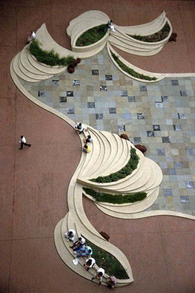 several people are walking around an artisticly designed area with benches and plants on the ground