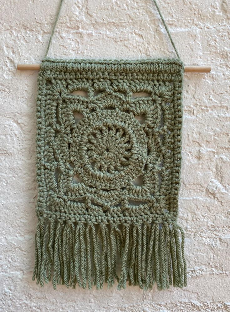 a green crocheted wall hanging with tassels on a wooden hanger