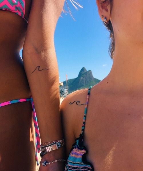 two women with tattoos on their backs standing next to each other in bikinis at the beach