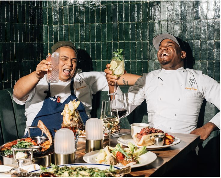 two men sitting at a table with food and drinks